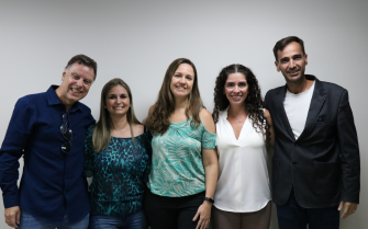 Três mulheres e dois homens estão lado a lado, sorrindo para a foto.