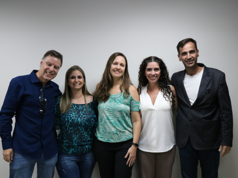 Três mulheres e dois homens estão lado a lado, sorrindo para a foto.