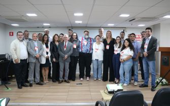 Participantes, homens e mulheres do evento, posam para a foto, lado a lado, no palco do auditório.