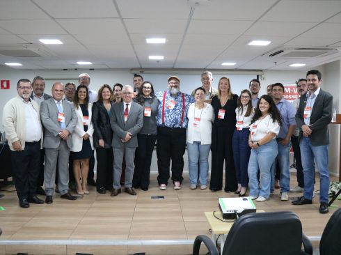 Participantes, homens e mulheres do evento, posam para a foto, lado a lado, no palco do auditório.