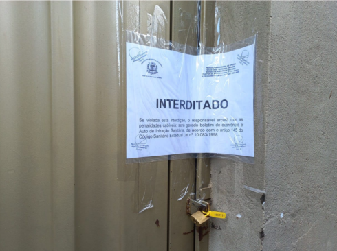 Imagem mostra um portão bege com um cartaz branco da Vigilância Sanitária de Limeira com a palavra Interditado e um lacre amarelo no cadeado