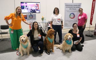 3 mulheres em pé sorrindo para foto atrás de 3 cães golden retriever sentados entre duas mulheres também sorrindo para foto.