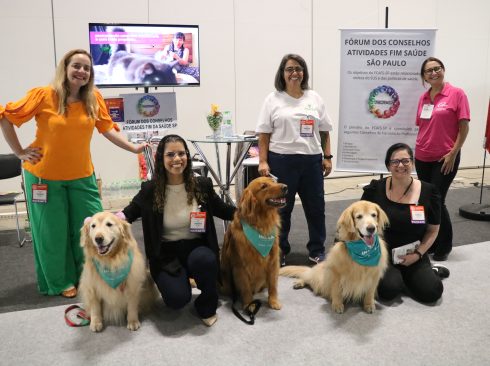 3 mulheres em pé sorrindo para foto atrás de 3 cães golden retriever sentados entre duas mulheres também sorrindo para foto.