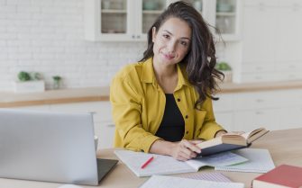 mulher sentada à mesa com livros, cadernos e notebook.