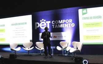No palco do evento, Lucas Figueiredo, gerente de Comunicação do CFMV, de terno e tênis, fala ao microfone, durante o lançamento do Prêmio CFMV/CRMVs de Jornalismo.
