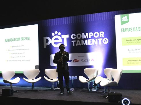 No palco do evento, Lucas Figueiredo, gerente de Comunicação do CFMV, de terno e tênis, fala ao microfone, durante o lançamento do Prêmio CFMV/CRMVs de Jornalismo.