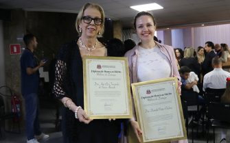 Duas mulheres posando para foto segurando placa de homenagem.