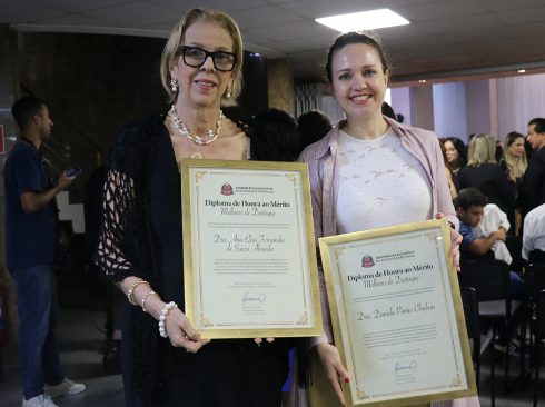 Duas mulheres posando para foto segurando placa de homenagem.