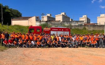 Equipe formada por profissionais de diversos setores, entre mulheres e homens posam em três fileiras em frente a um carro do Corpo de Bombeiros