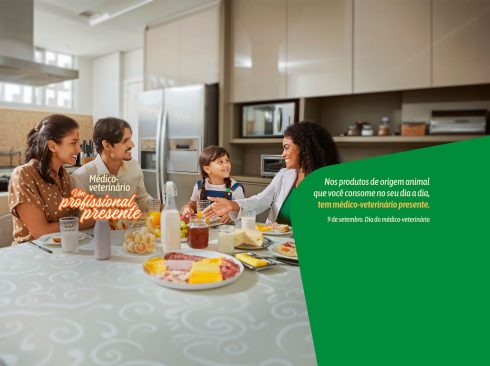 Imagem de homenagem ao Dia do Médico-Veterinário com pessoas sentadas em volta de uma mesa de refeição em uma cozinha e diferentes tipos de alimentos de origem animal sobre a mesa.