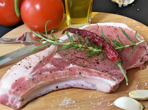 Imagem de um pedaço de carne de porco, com tomates e azeite ao fundo.