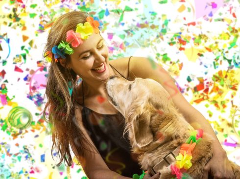 Em cenário carnavalesco, tutora sorri com seu cachorro no colo